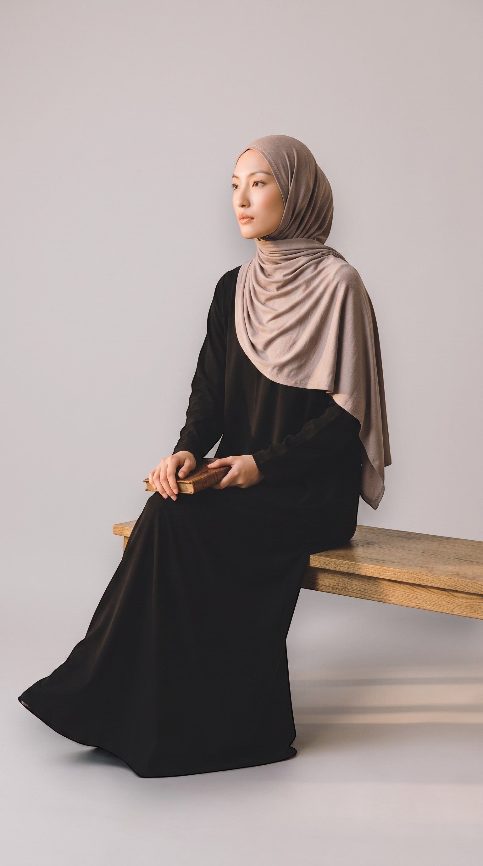 Eternal Aura soft beige jersey hijab worn by a woman in a black dress sitting on a wooden bench