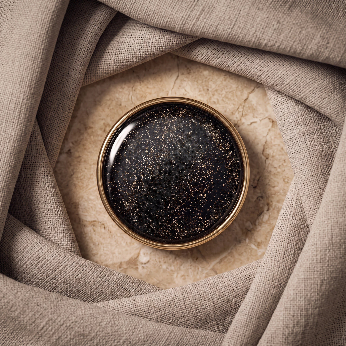 Eternal Aura round hijab magnet in black with gold glitter detail, set against beige fabric folds.