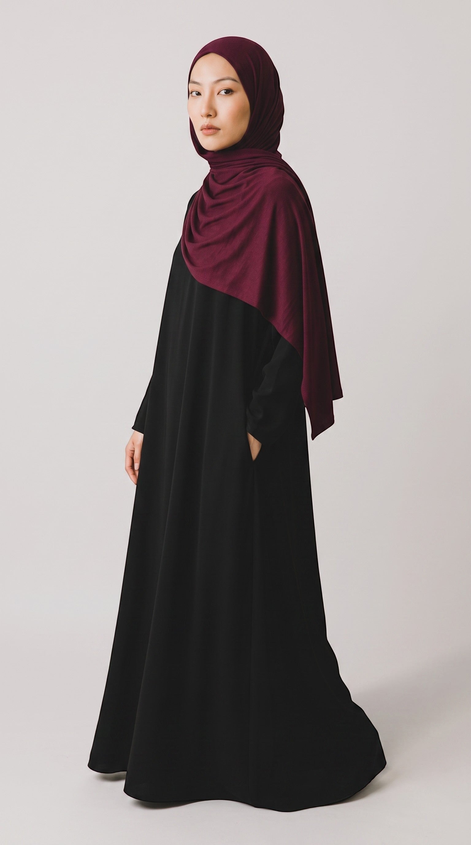 Eternal Aura jersey hijab in deep burgundy worn by a model in a black abaya against a neutral studio background
