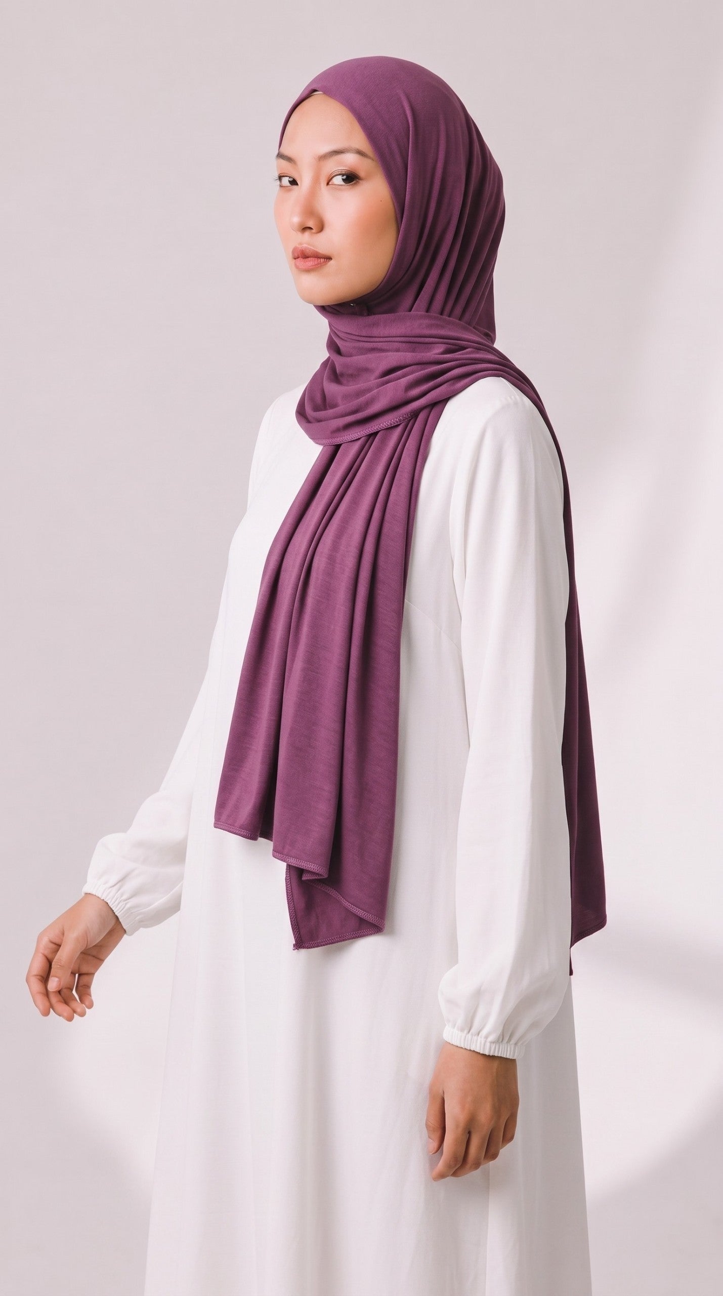 Model trägt ein dunkelviolettes Eternal Aura Jersey-Hijab zu einem schlichten weißen langärmeligen Kleid