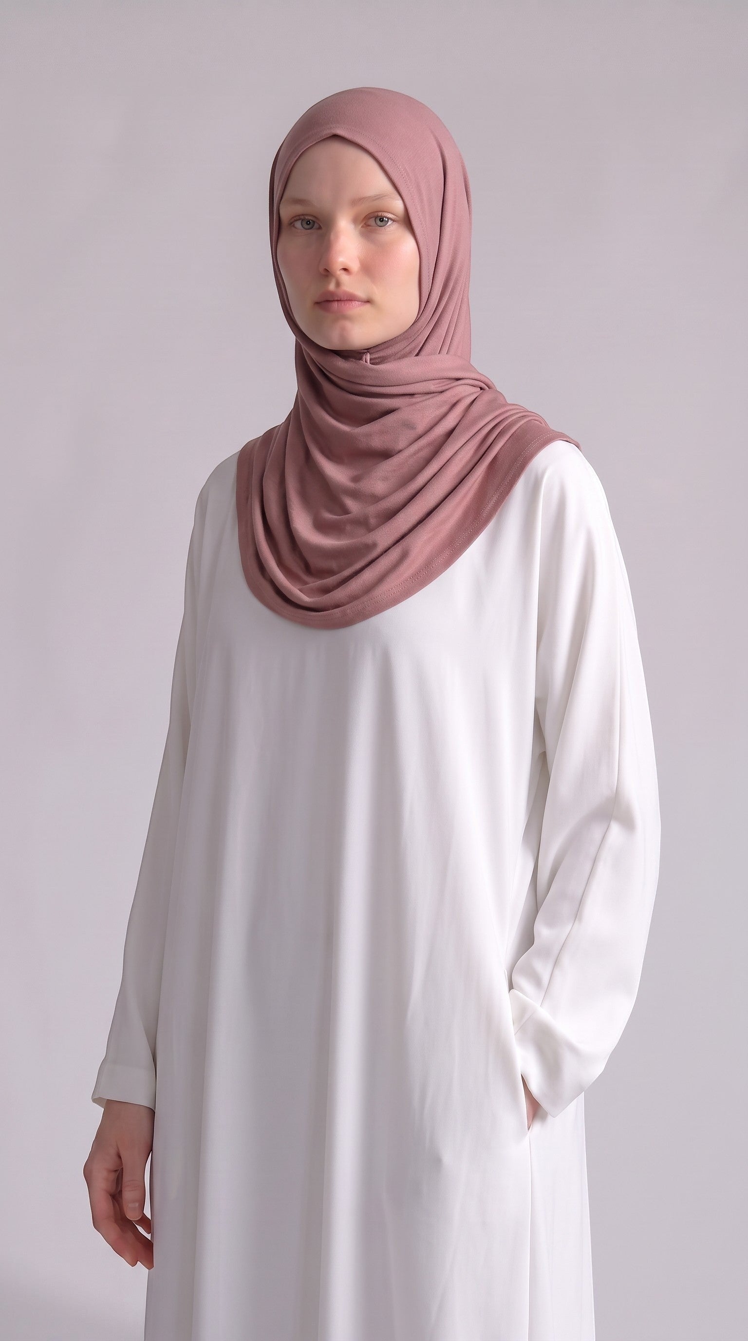 Model wearing a dusty rose Eternal Aura jersey hijab with a white long-sleeved dress against a neutral background