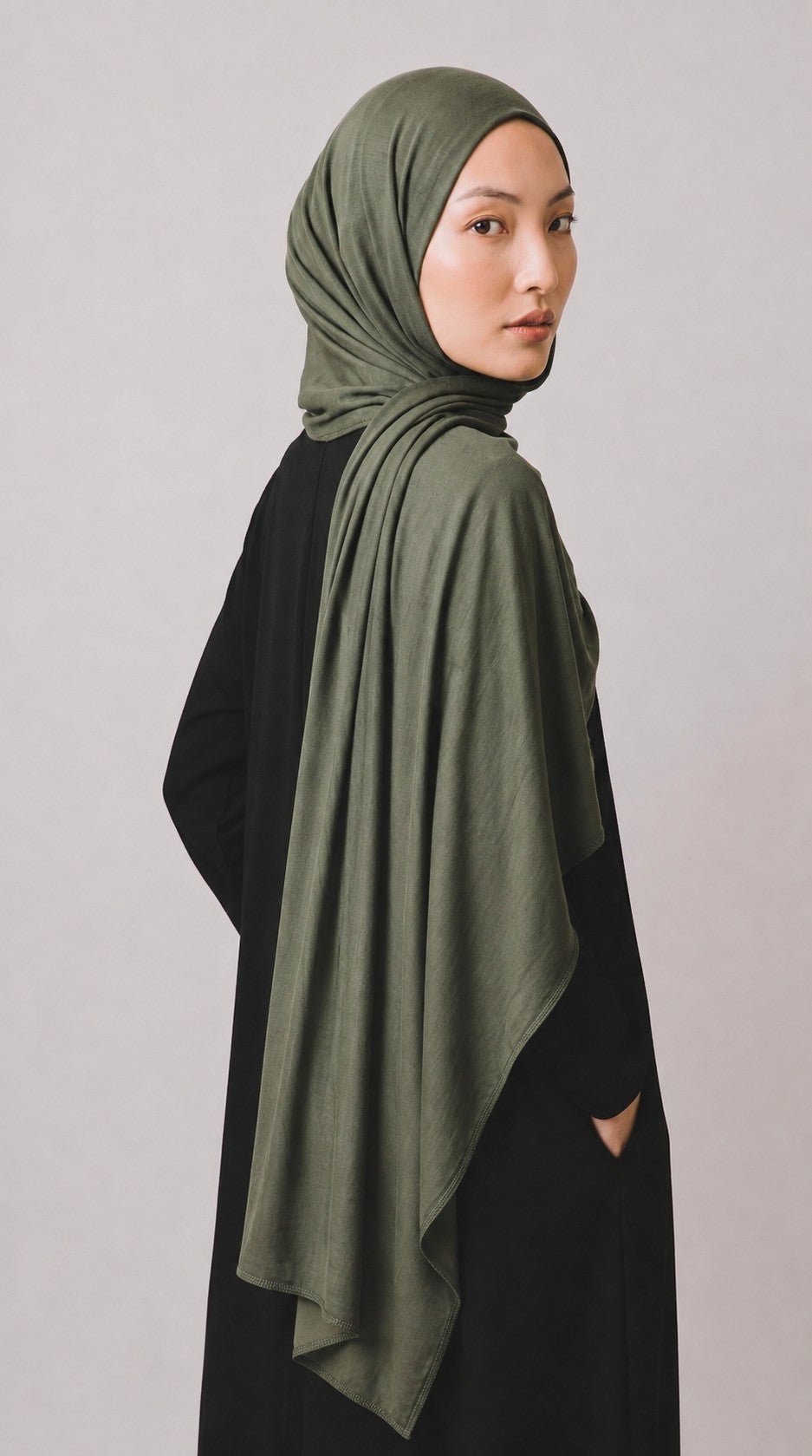 Model trägt ein olivgrünes Eternal Aura Jersey-Hijab zu einem schlichten schwarzen Kleid vor hellem Hintergrund