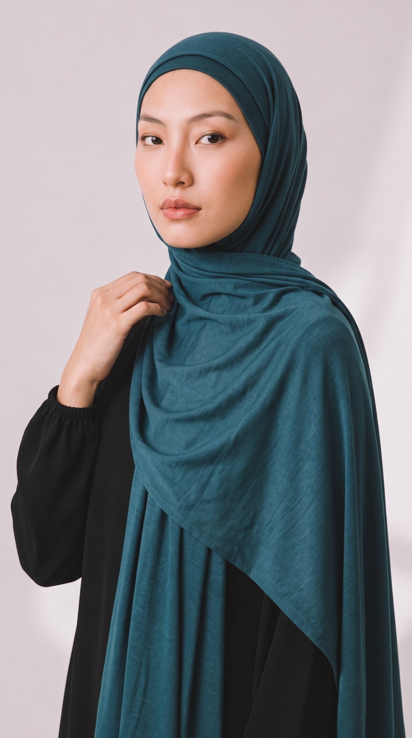 Model trägt ein petrolfarbenes Eternal Aura Jersey-Hijab aus weichem, fließendem Stoff vor hellem Hintergrund.