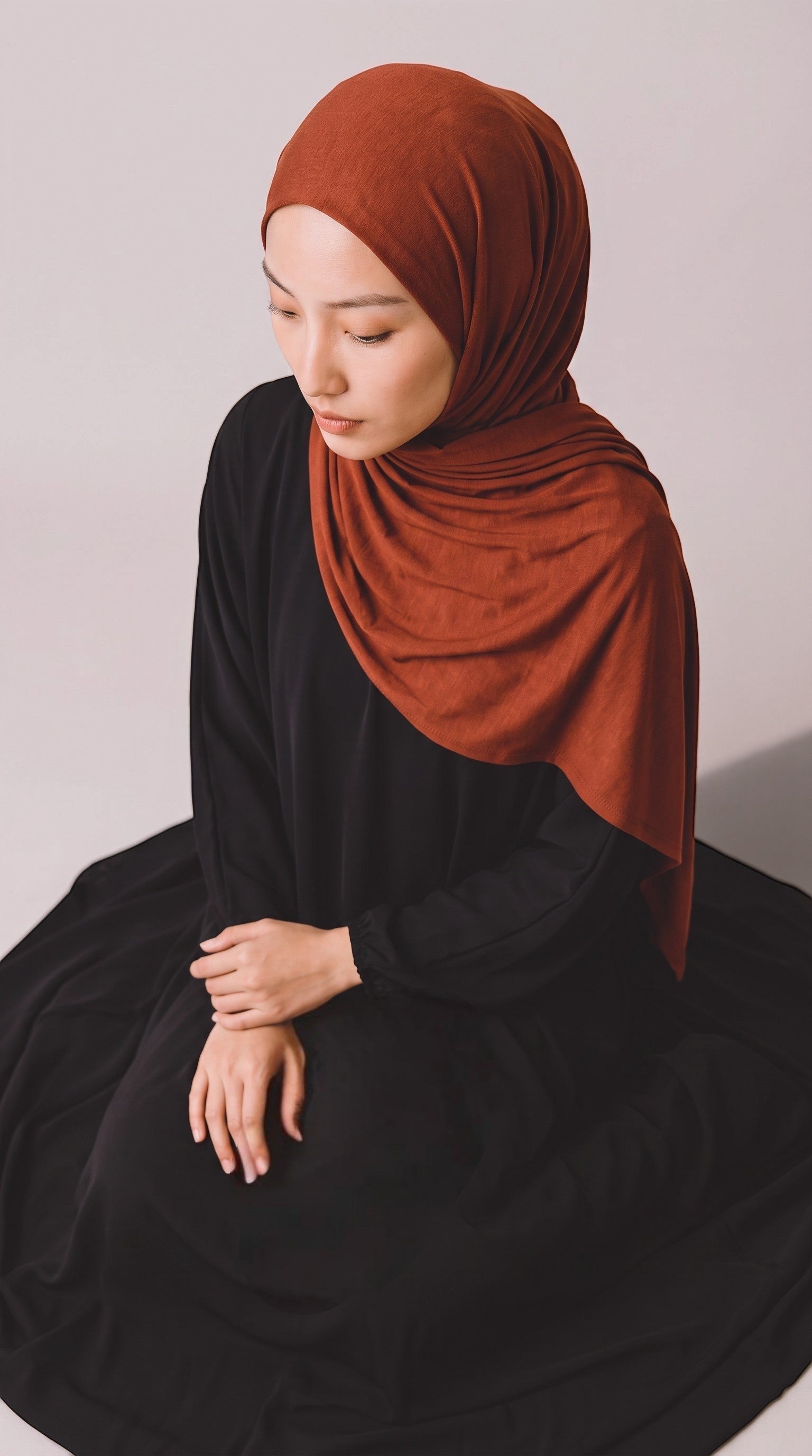 Eternal Aura jersey hijab in rust orange worn by a woman in a black dress against a neutral background