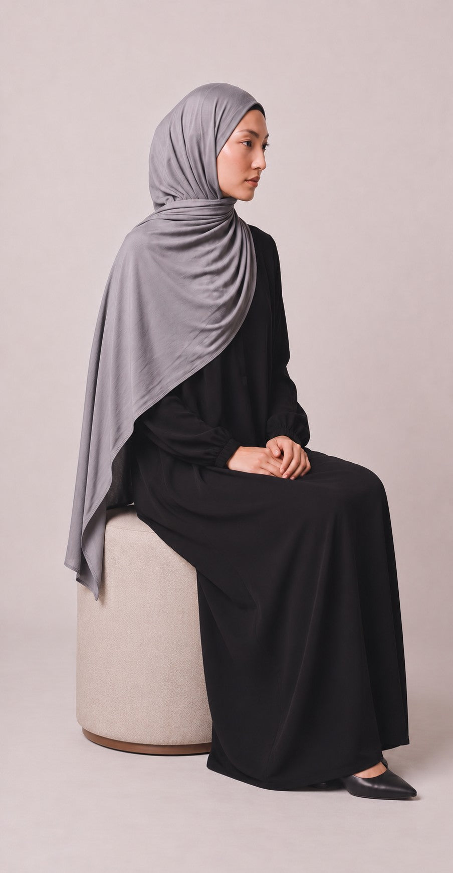 Eternal Aura Model trägt ein schlichtes schwarzes Abaya-Kleid mit einem eleganten grauen Jersey-Hijab im Studio
