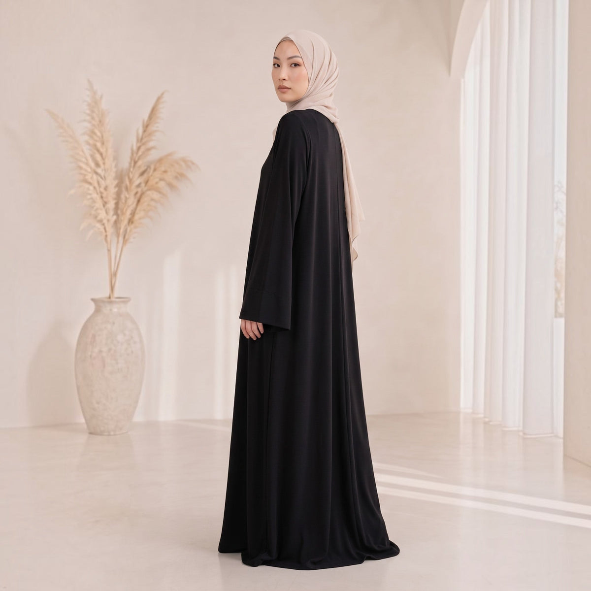 Model trägt eine elegante schwarze Eternal Aura Serein Abaya mit beigem Hijab in einem minimalistischen Studio-Setting.