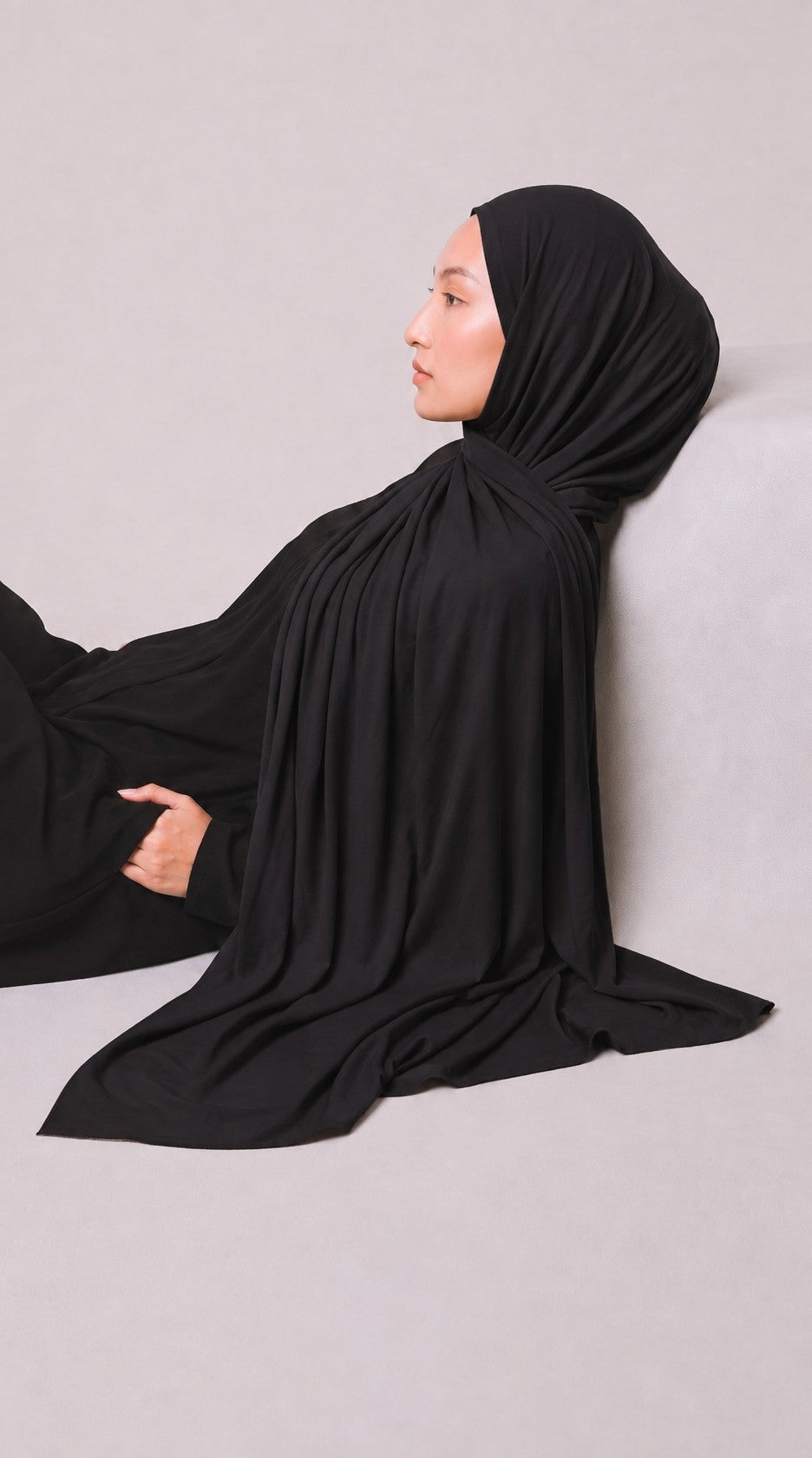 Eine Frau trägt ein elegantes schwarzes Eternal Aura Hijab aus weichem, fließendem Stoff in einer Seitenansicht.
