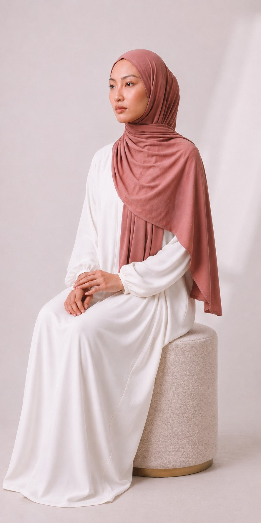 Eternal Aura Model trägt ein weißes langes Kleid mit einem altrosa Hijab in einer eleganten Studioaufnahme
